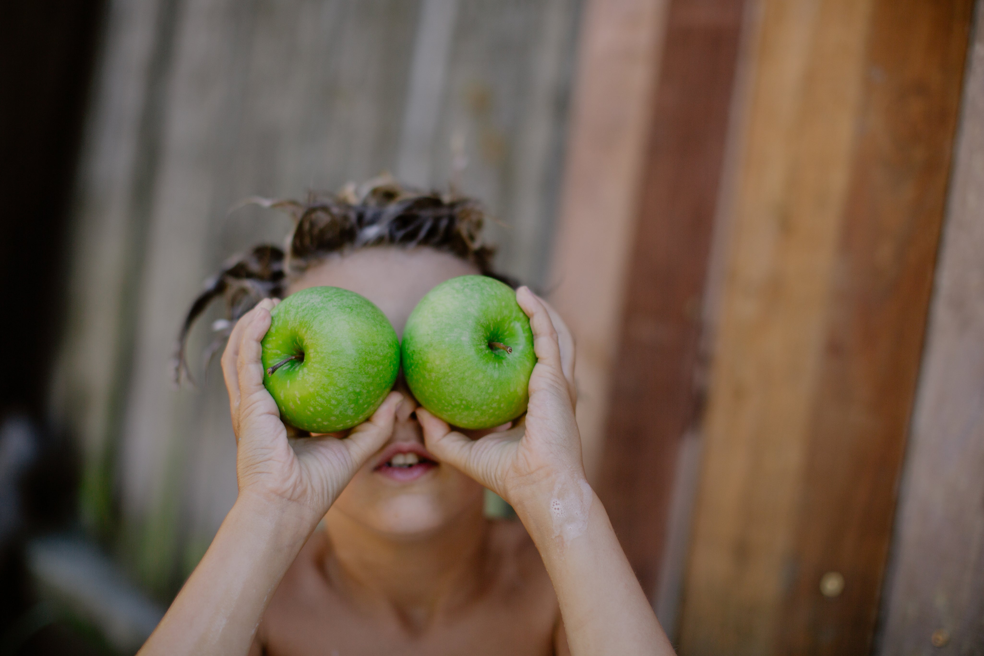 a boy holding 2 apples in front of his eyes