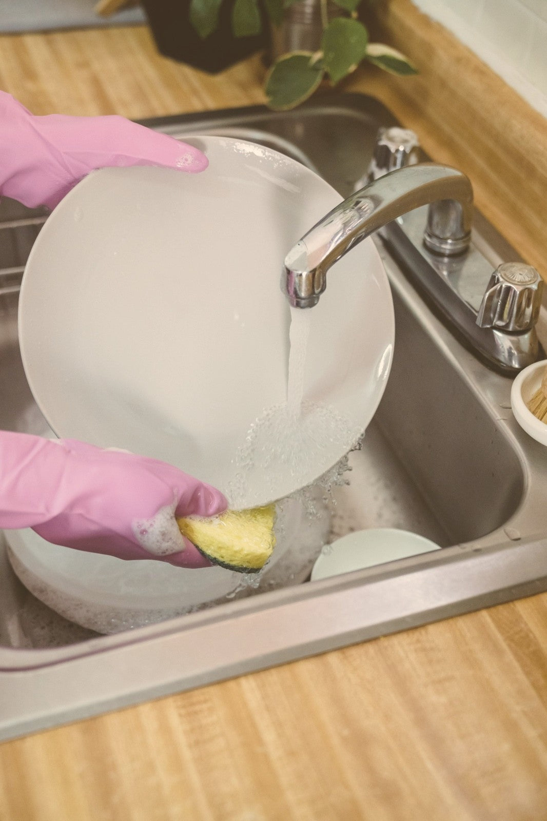 Dry hands from washing dishes: gloved hands rinsing a plate under a warm tap