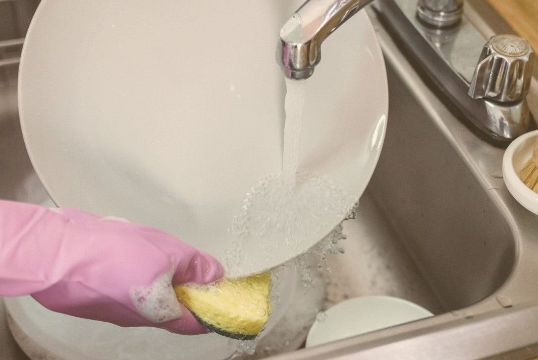 Dry hands from washing dishes: gloved hands rinsing a plate under a warm tap