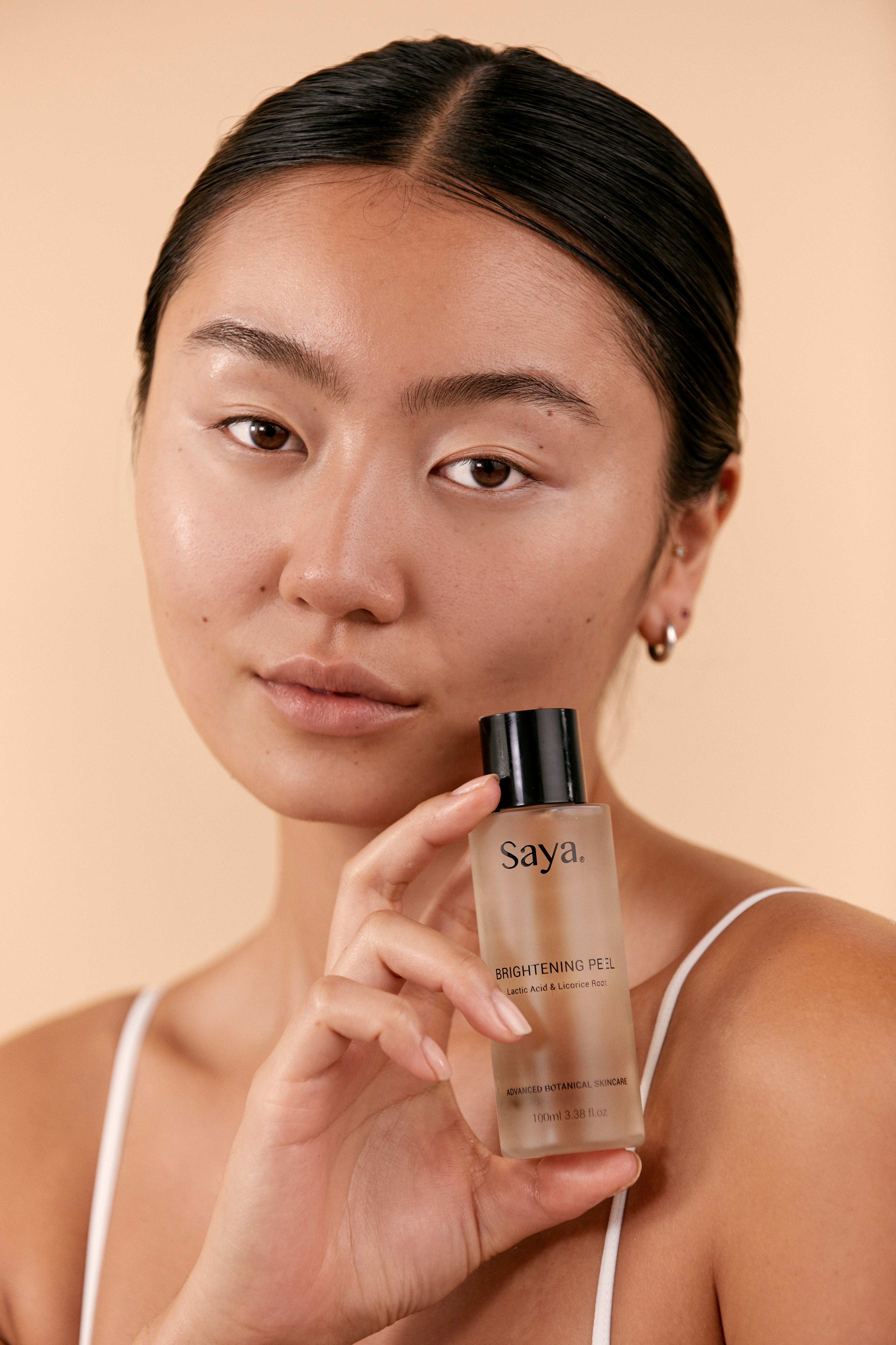 a woman holding a bottle of saya brightening peel