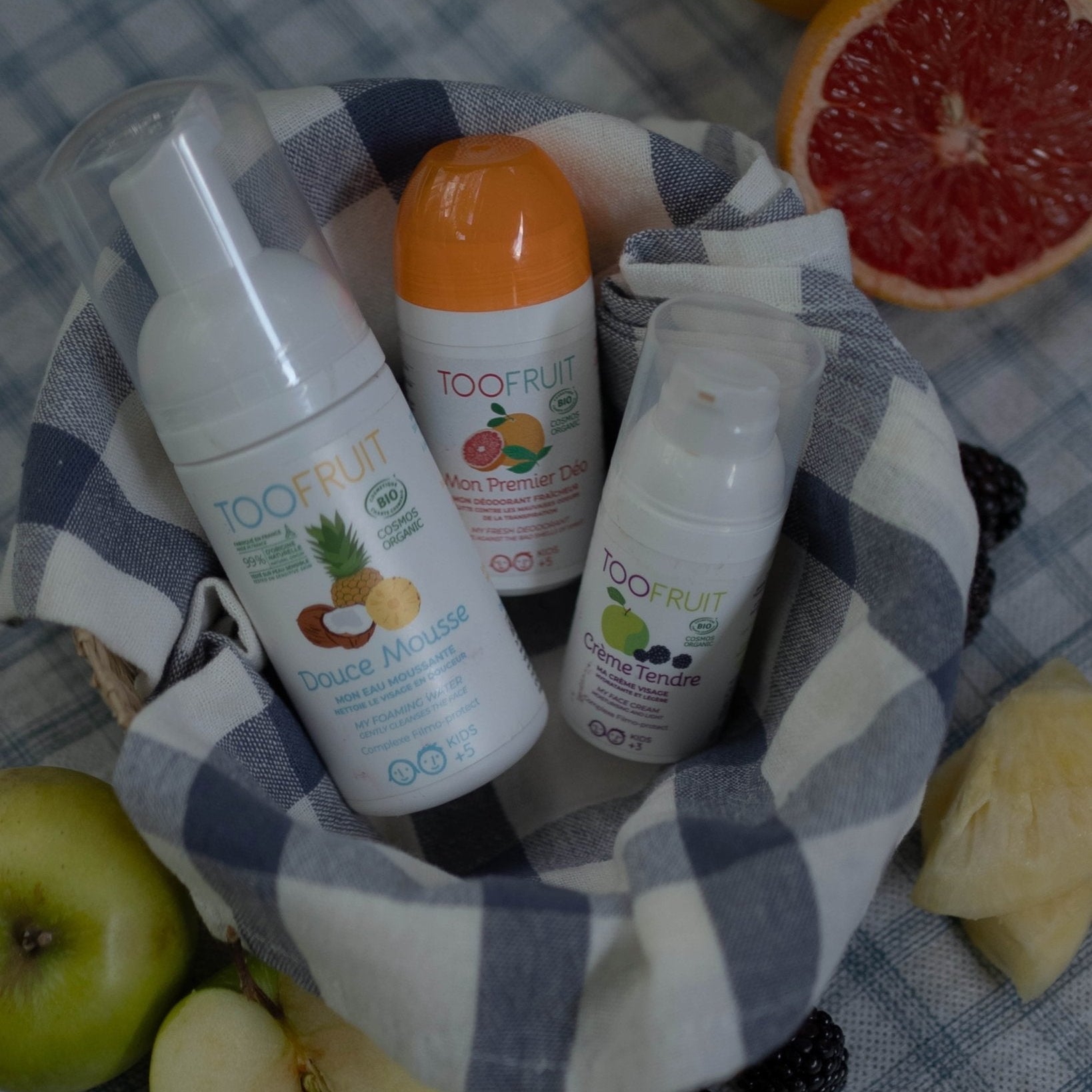 Basket with 3 TOOFRUIT products on a checkered tablecloth with fruits around.