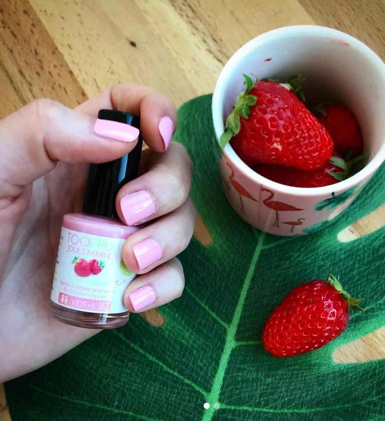 a hand holding a bottle of toofruit strawberry nail polish and strawberries